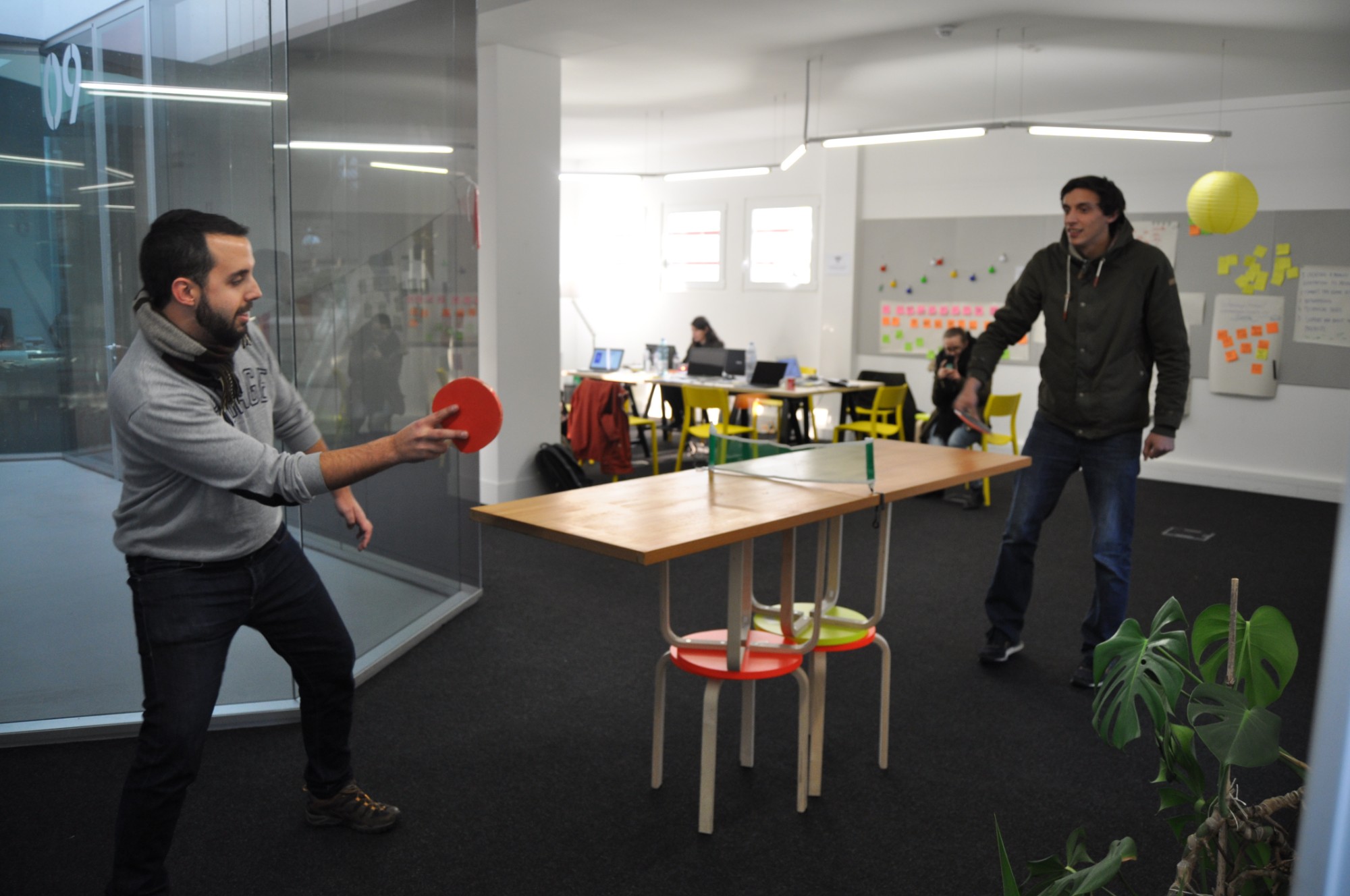 Two students play ping pong on a table made from desks and stools in the studio