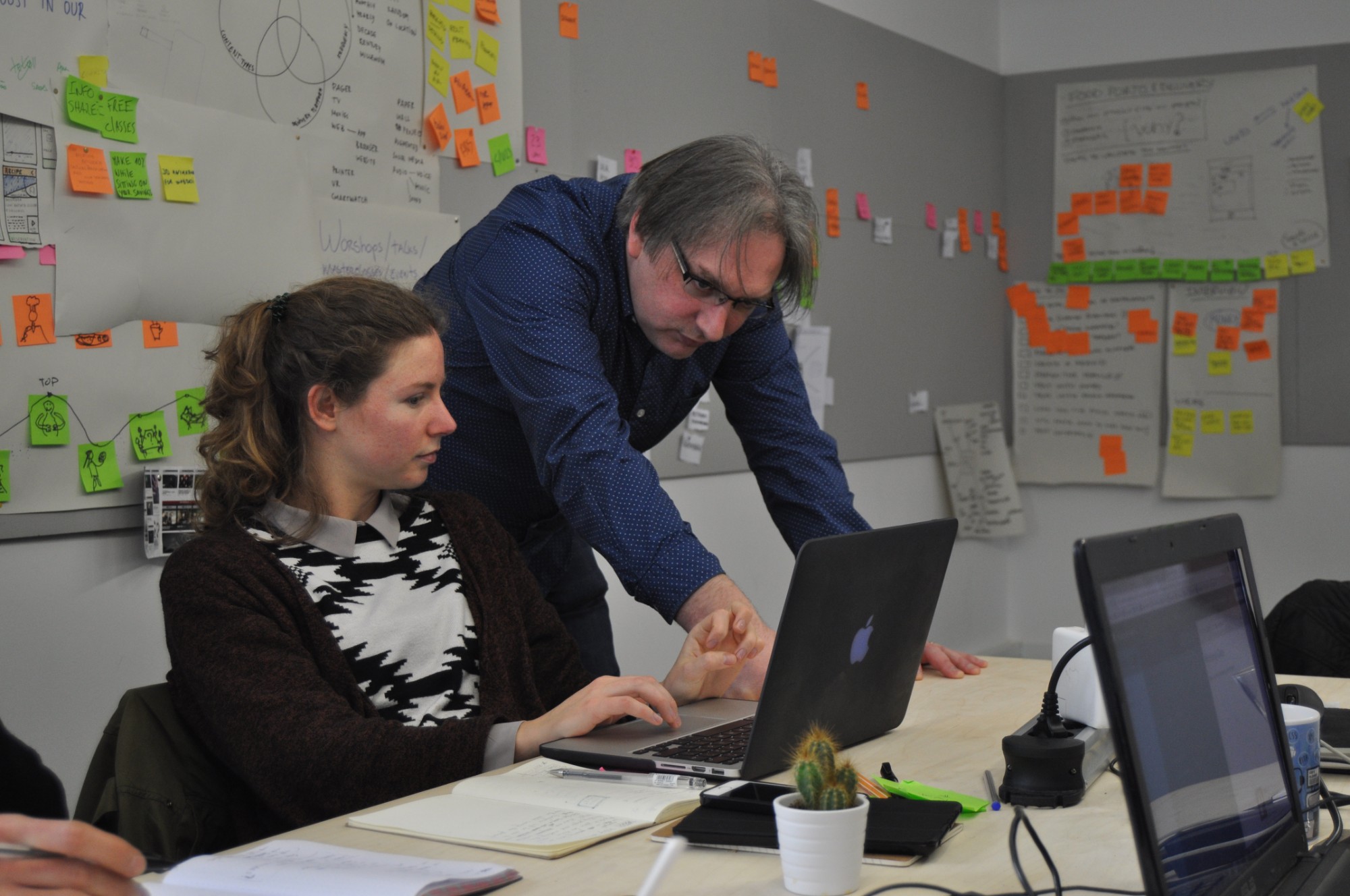 Jeremy Keith leans over a student's laptop during his masterclass, in front of a wall of sticky notes