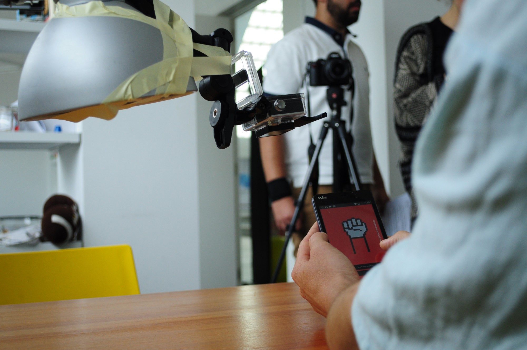 A user tests the Democracy Squared app on a phone while cameras taped to a lamp and on a tripod record the session