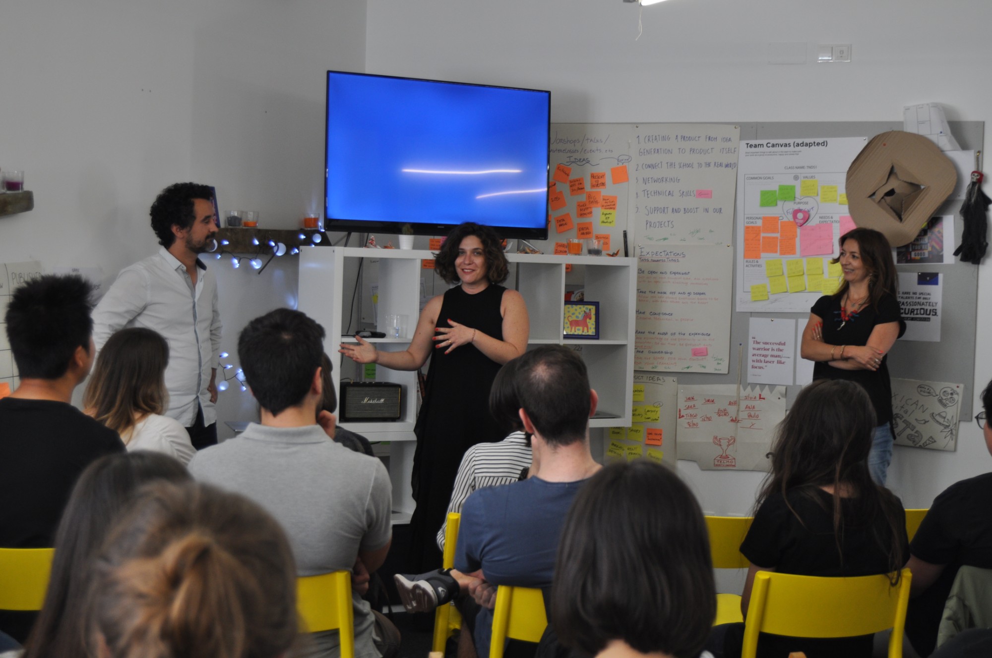 Three guest speakers talk to an audience on yellow chairs at an event in the TNDS studio