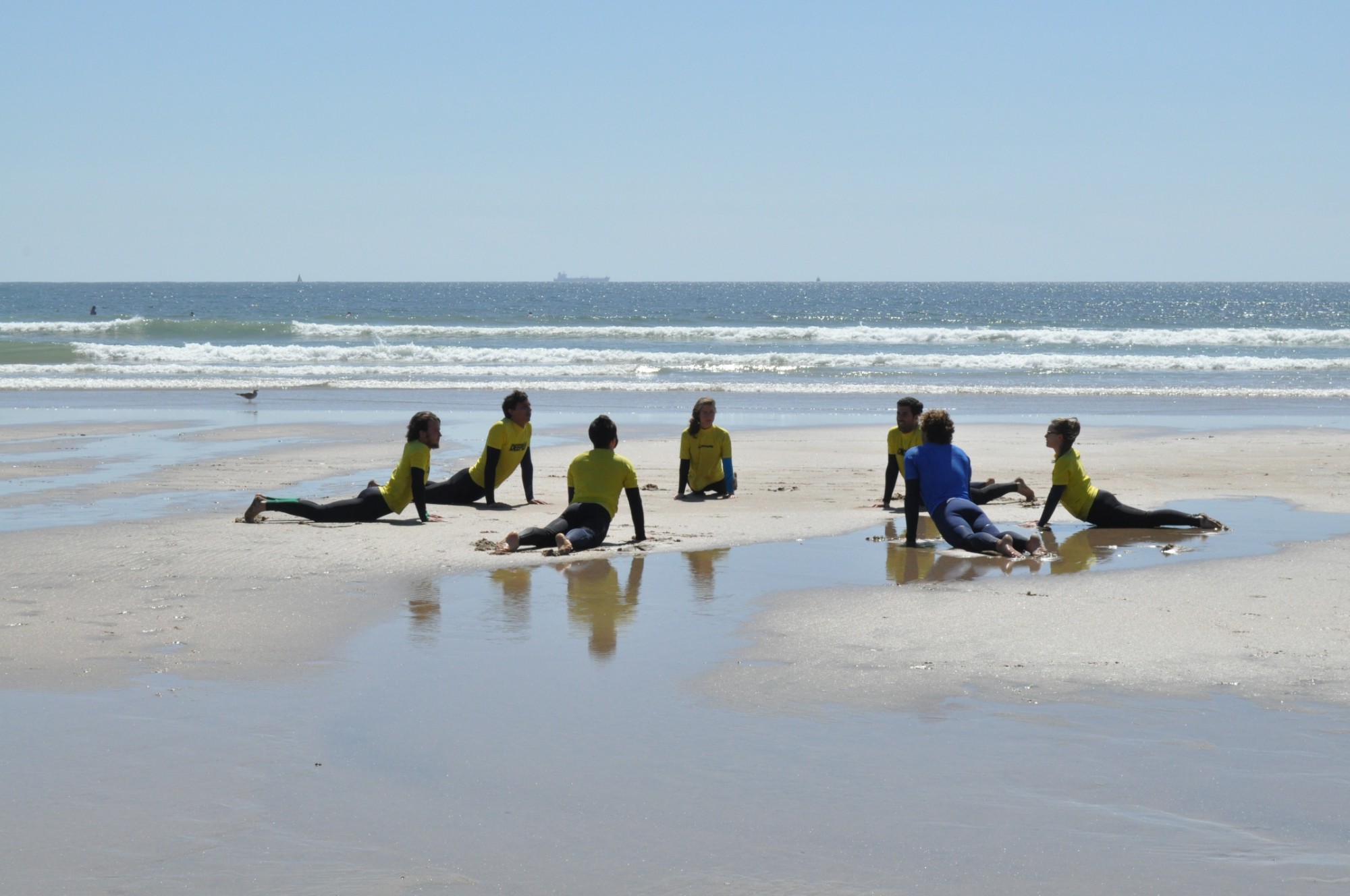 Students in wetsuits stretch on the sand with their instructor before a surf lesson