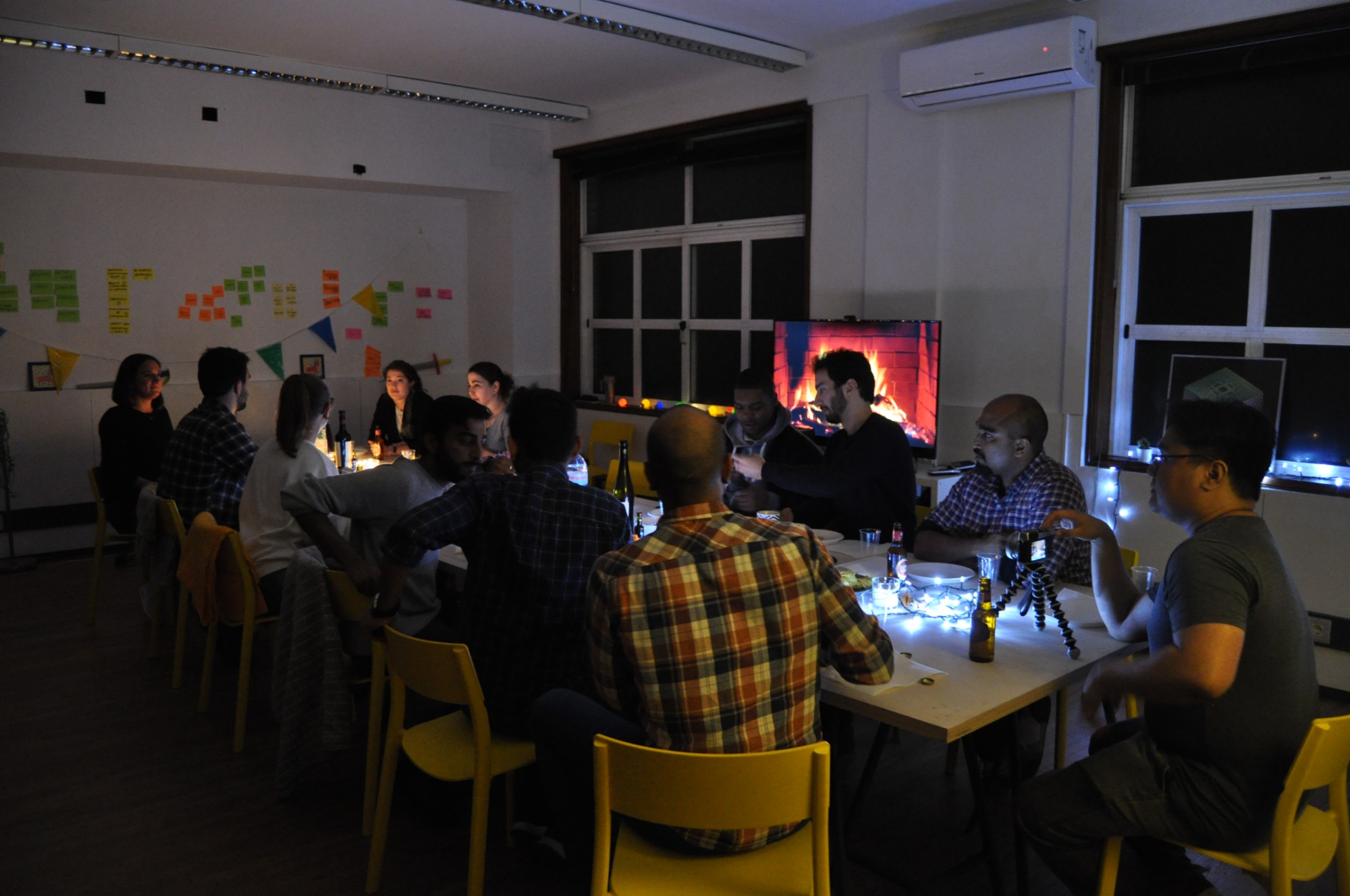 Students share a candlelit dinner at long tables in the studio, with a fireplace video playing on the screen