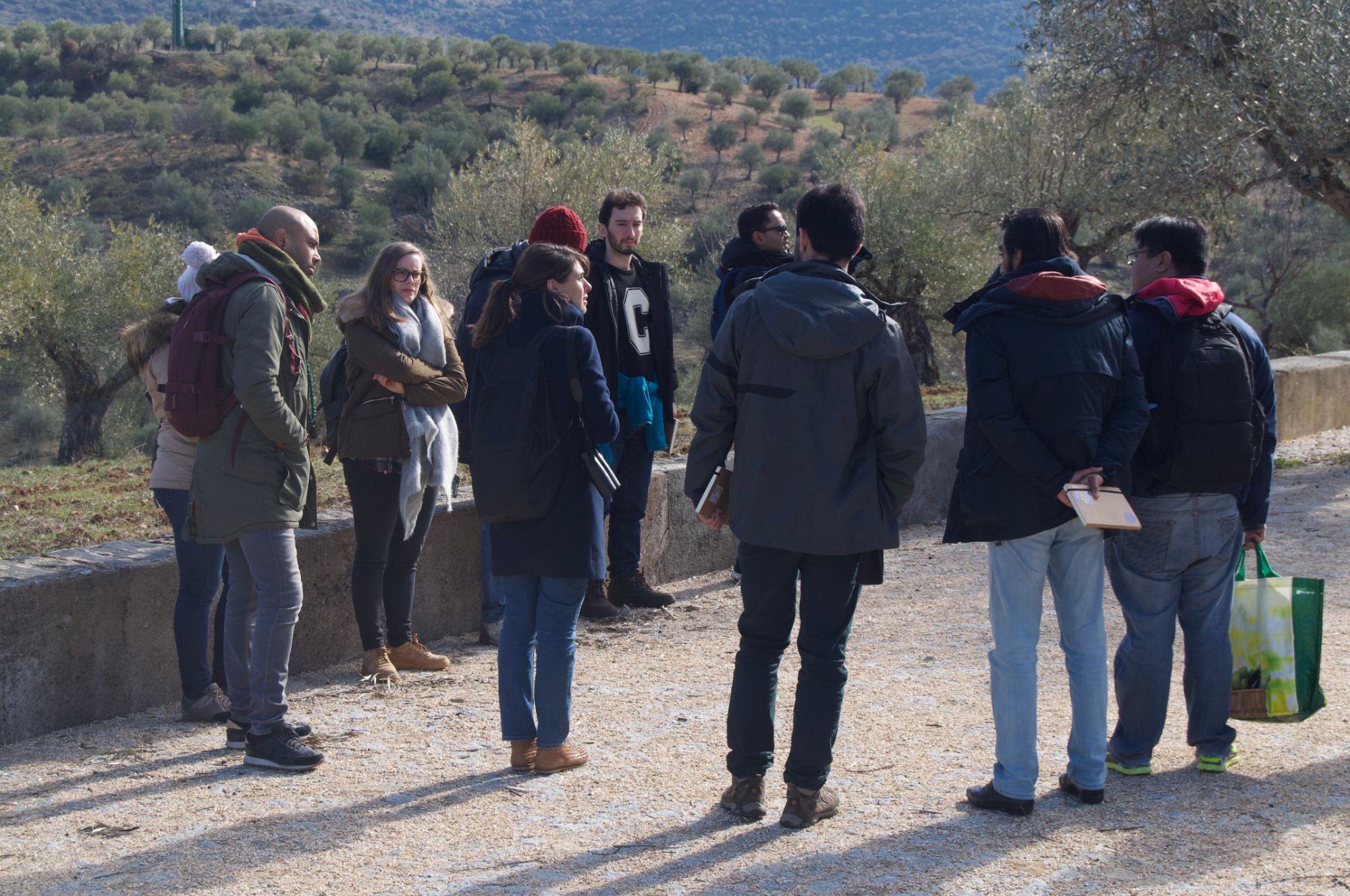 Students in winter coats gather on a hillside road among olive groves during the field trip near the Spanish border